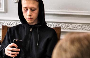 A boy with sunken eyes looks at a mobile phone