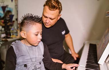 A man sits with a boy at a piano