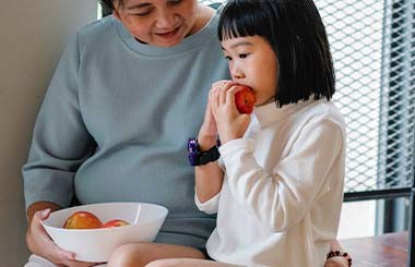 A girl is eating an apple next to a woman