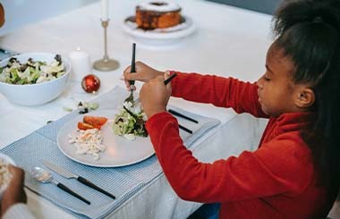 A girl is sat at a dining table with a plate of food in front of her