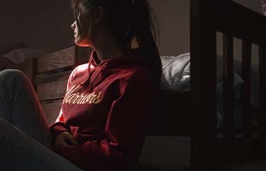 A girl sits in a dark bedroom