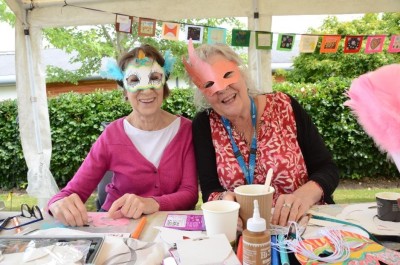 Two women smile whilst wearing masks they have created during an art session.