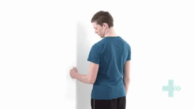 Moving image of someone with their elbow bent, facing a doorframe. They are pushing their hand inwards against the wall at the side of the doorway.