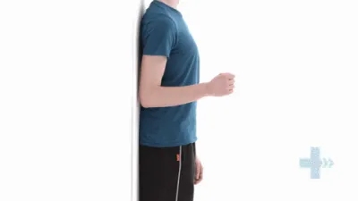 Moving image of someone with their elbow bent, back to a wall. They are pushing their elbow backwards against the wall