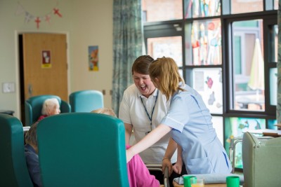 Two healthcare workers speak and laugh with service users on a ward.